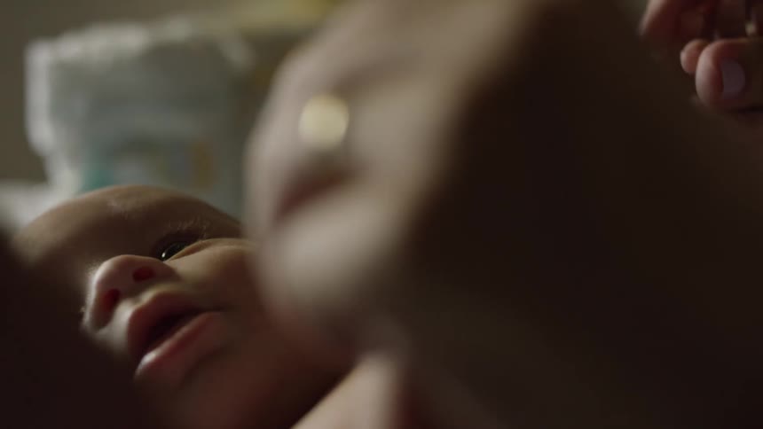 An infant lies on the bed while an adult holds both of the babys hands playfully interacting with them