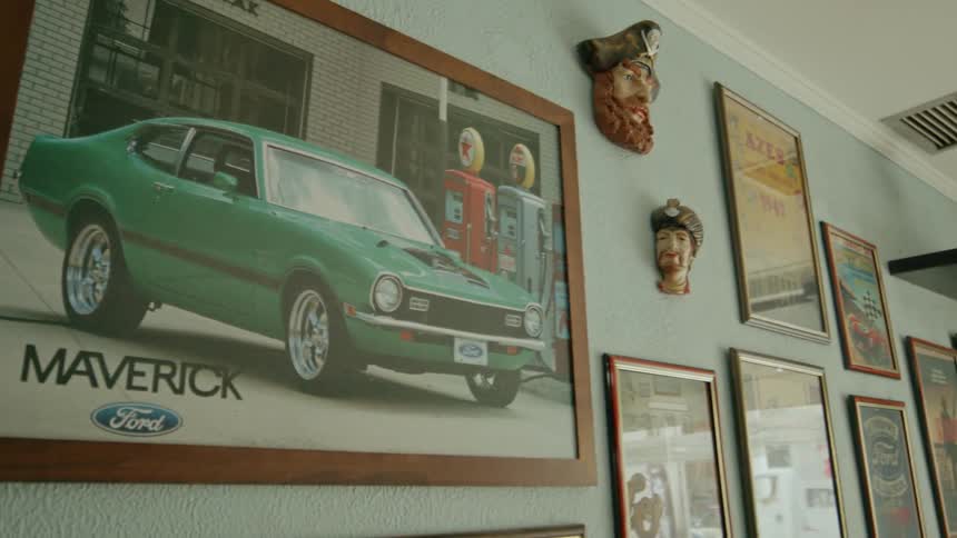 A picture frame containing an image of a green car is mounted on a wall alongside other frames
