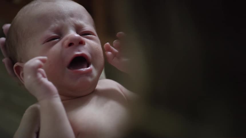 Close up of a baby crying in a persons arms