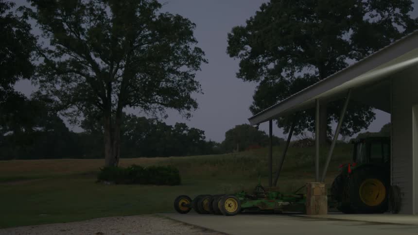 Farm equipment sits near a barn at dawn