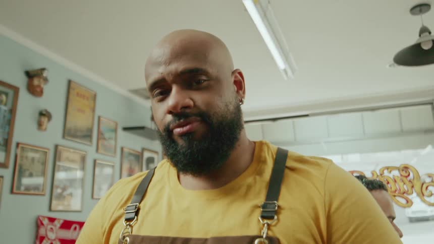 The barber is smiling and tapping his razor on his hand