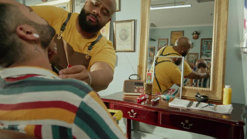 A barber cleans the face of a man whose hair he just finished cutting inside a barbershop at midday
