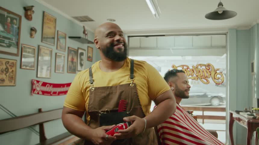 A black barber standing next to a customer both are smiling and laughing