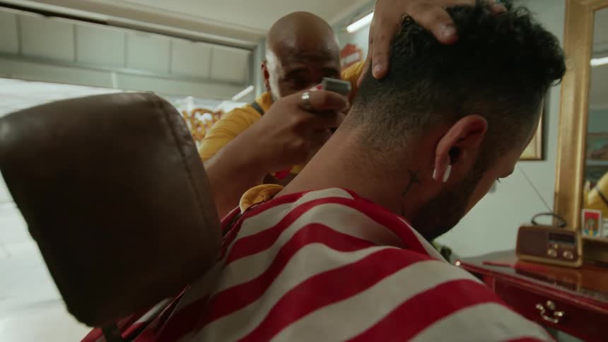 Barber cutting a mans hair with a clipper inside the barber shop in the morning