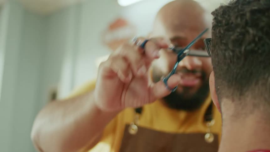 Barber trims a client hair with scissors in a closeup shot