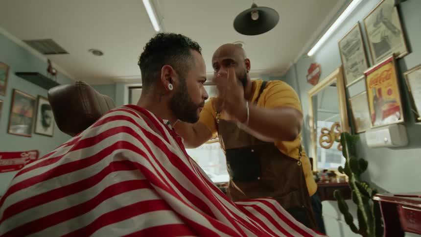 A barber enthusiastically cuts another mans hair in his barbershop at midday