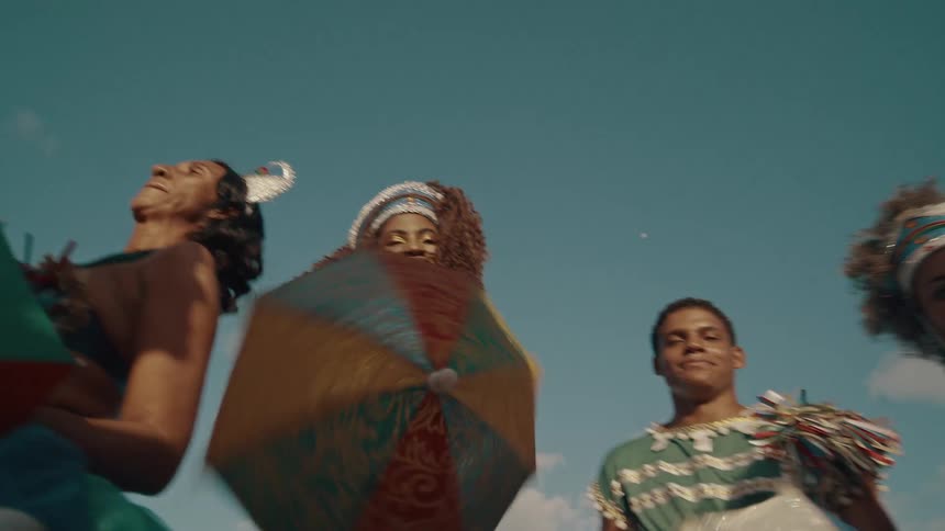 A group are dancing in colorful costumes on a sunny day