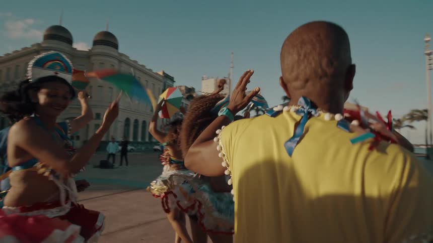 People in festive costumes joyfully dance in a sunlit city square