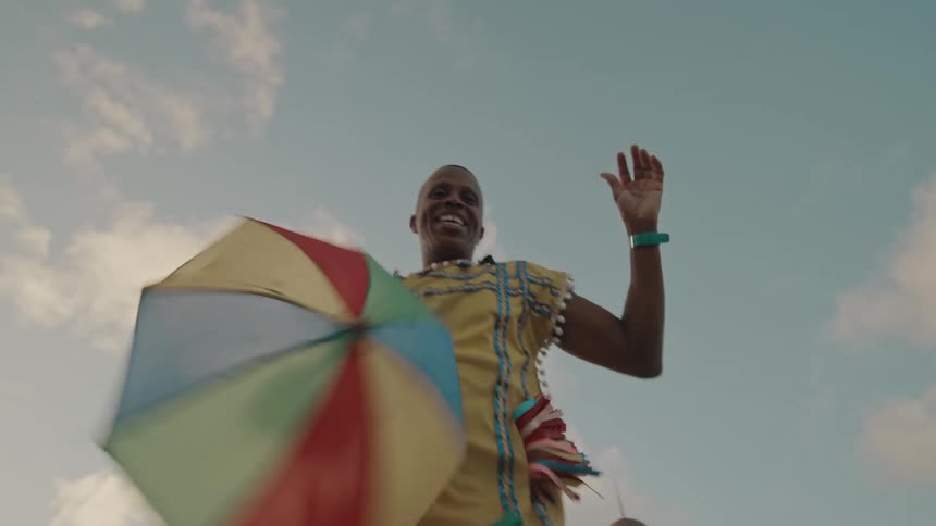 Dancing man holding a small colorful umbrella and dancing in a typical yellow outfit