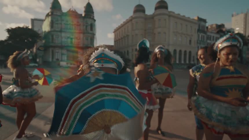 A group of dancers in vibrant traditional costumes with small colorful umbrellas begin a performance in a historic city square