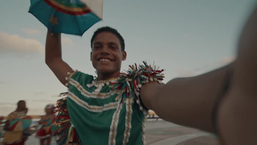 A man wearing a colorful outfit is holding an umbrella outdoors and dancing
