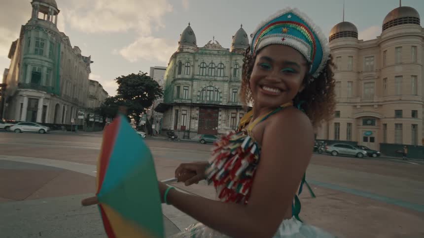 A black female wearing a colorful costume is smiling and twirling an umbrella