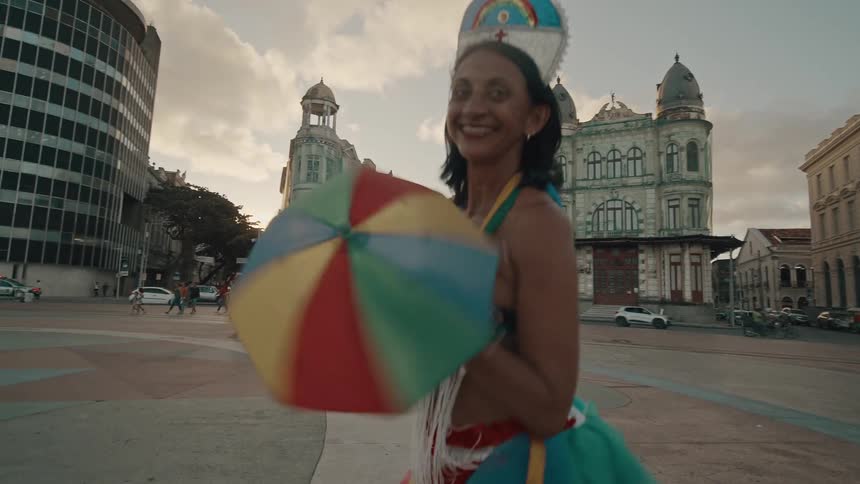 Woman in a square with a happy expression and wearing typical carnival clothing dancing
