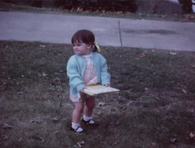 An older film of a child carrying a book around in the yard