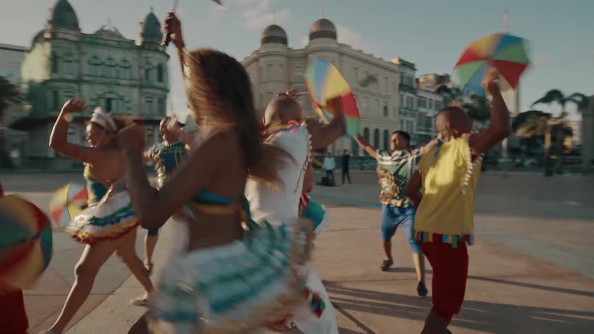 A vibrant group of dancers in colorful traditional costumes joyfully celebrate in a historic city square waving small multicolored umbrellas