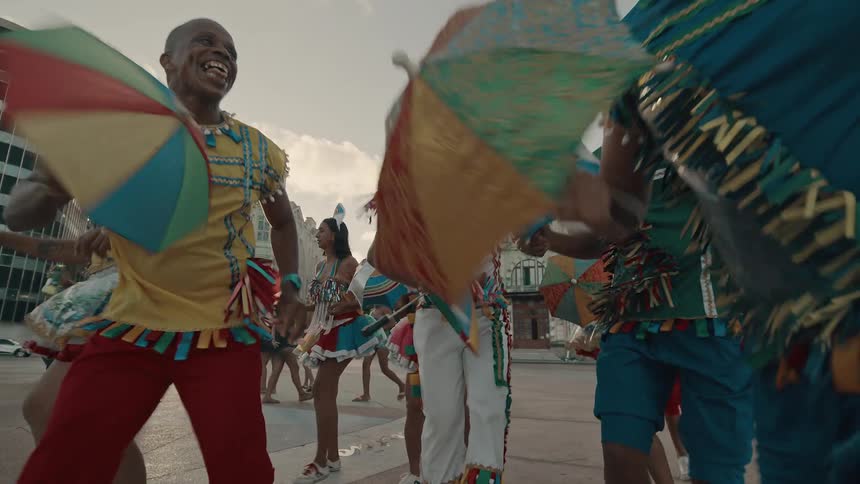 A group of people in native african attire dance in the middle of the street at midday