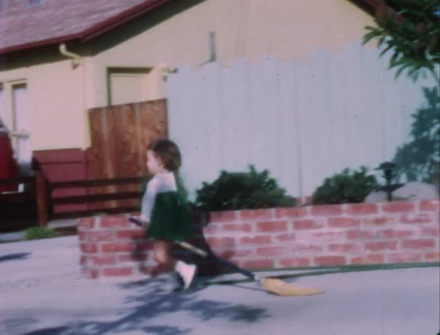 A young toddler walks outside dragging a broom