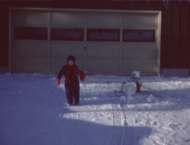 A child pulling its sibling on a sled in the snow in their driveway