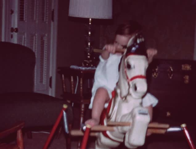 A girl is riding her toy in the living room