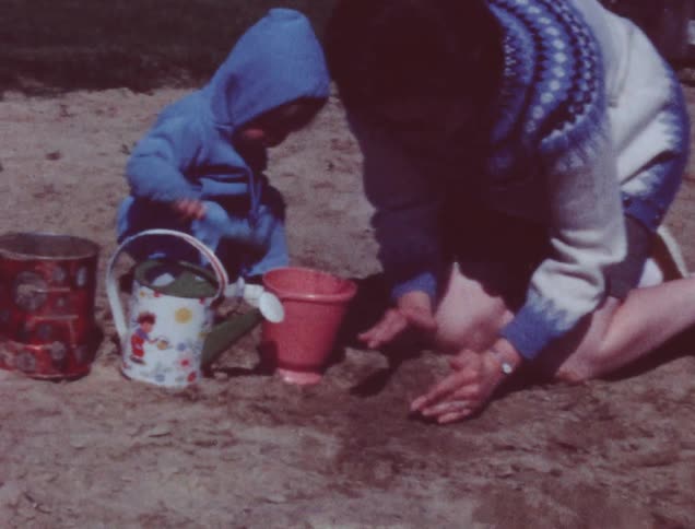A woman kneels to play with a toddler in the sand
