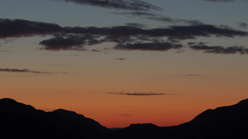 Silhouetted mountains under a colorful sky at dusk with scattered clouds