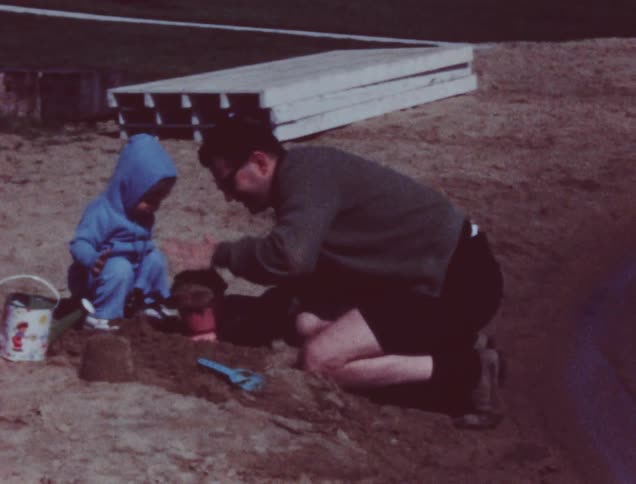 Man and child play in the sand with buckets