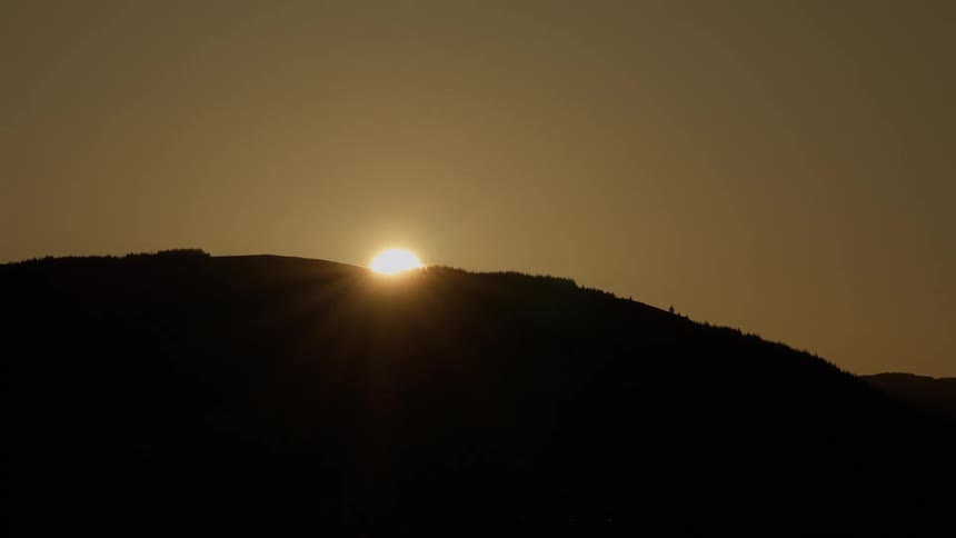 Sun setting on the horizon below the hillside