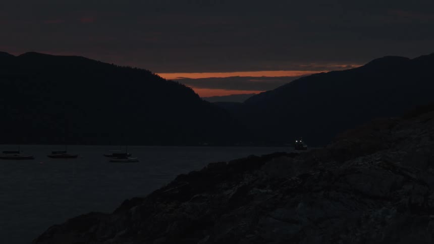 A lake view at night with boats docked near the shore and mountains in the background
