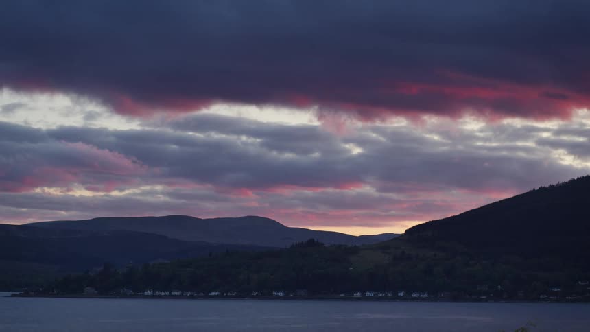 A purple pink dusk sky glows over mountains and a calm lakeside town