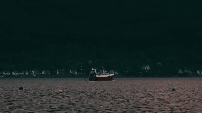 A fishing boat floats calmly on a quiet lake near a dark forested shoreline at dusk