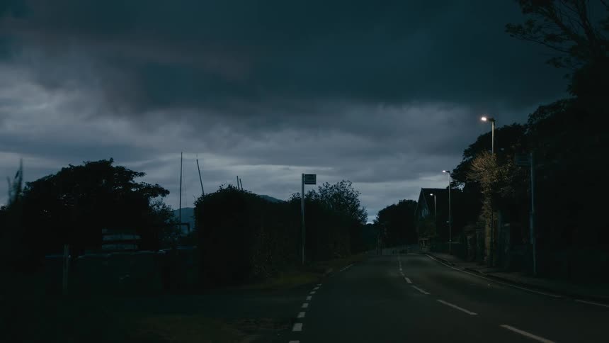 A dark moody road scene under stormy skies just before nightfall