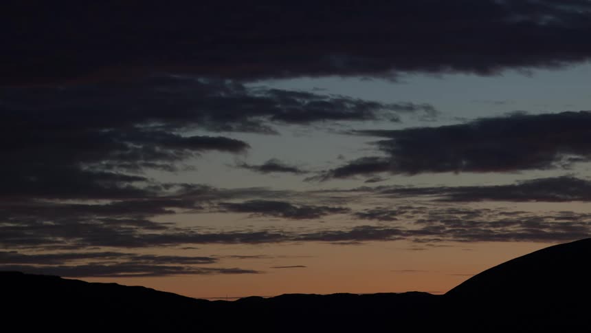 The sky at dusk features a band of orange light above dark mountains with multiple layers of grey clouds overhead