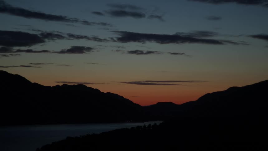 Silhouetted mountains and a calm lake at dusk under an orange blue sky