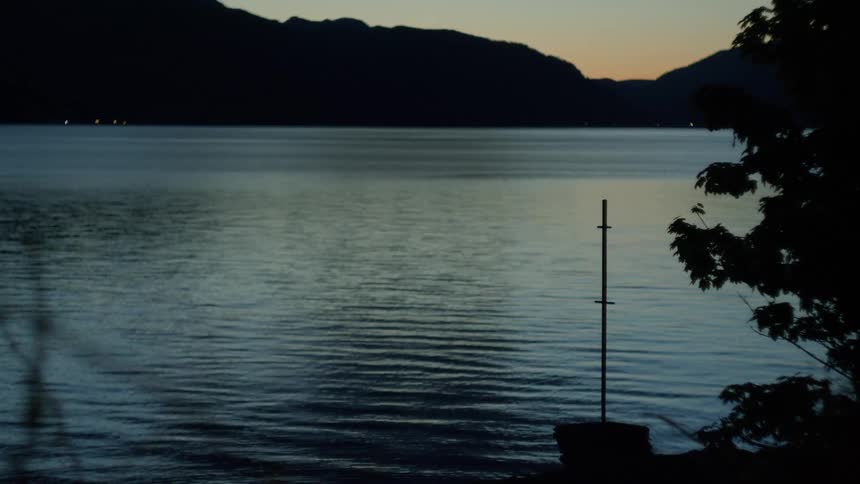 A peaceful lake reflects soft twilight hues as mountains silhouette the horizon