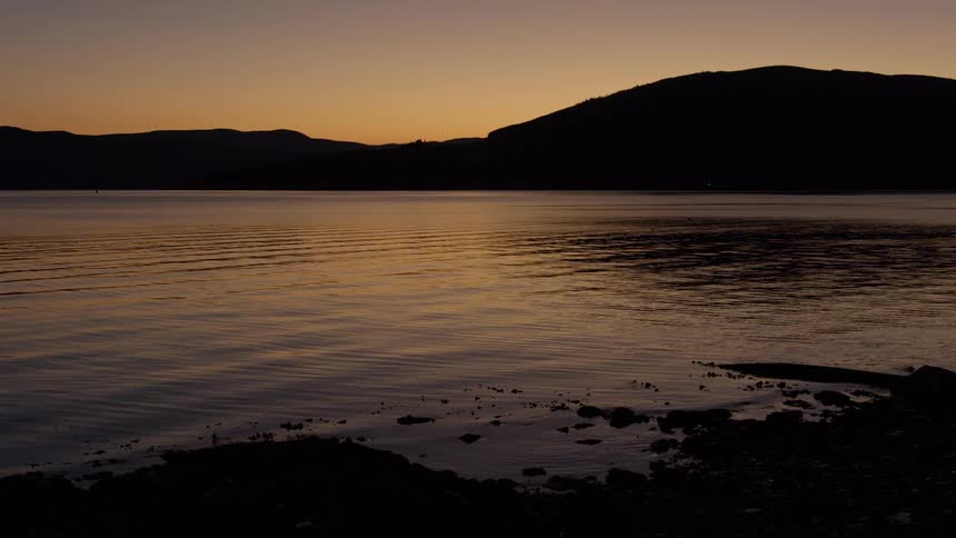 Golden dusk over calm lake with silhouetted hills