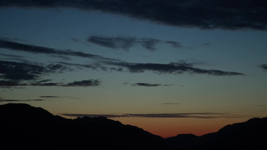 Silhouetted mountains rest beneath a colorful dusk sky with scattered clouds