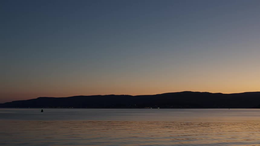 An ocean view with a shoreline surrounded by mountains at sundown