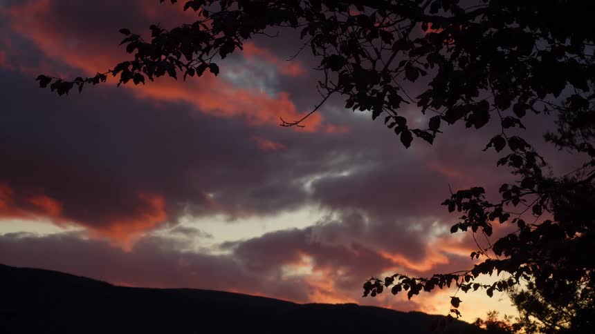 The sky at dusk with orange colors surrounding clouds with a landscape in the background