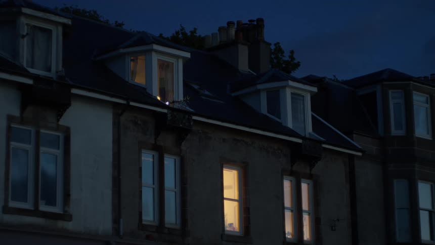 A dark residential building at night with a few warmly lit windows glowing