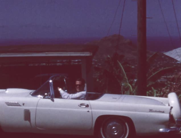 A man waves and drives away in a white car