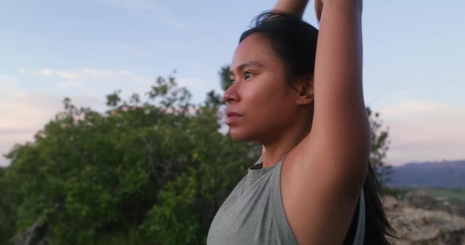 A woman stretches outdoors in front of trees during sunset