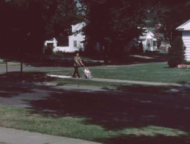 Man pushing child in stroller on neighborhood sidewalk on sunny day