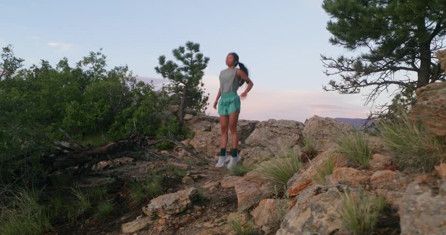A woman warms up before her workout on a rocky trail surrounded by trees in nature