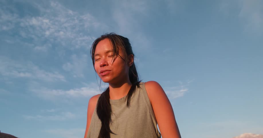 A young woman catches her breath after a run on top of a rocky mountain at midday