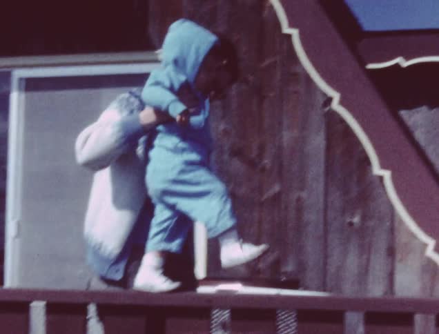 A woman holding a child as they walk across the railing in front of their house