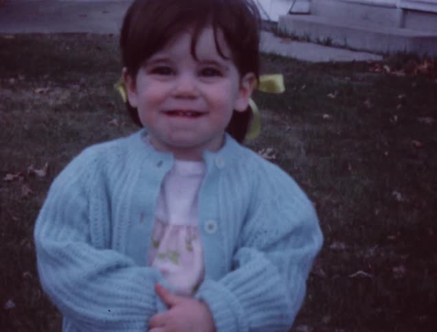 A young girl stands on grassy lawn and smiles