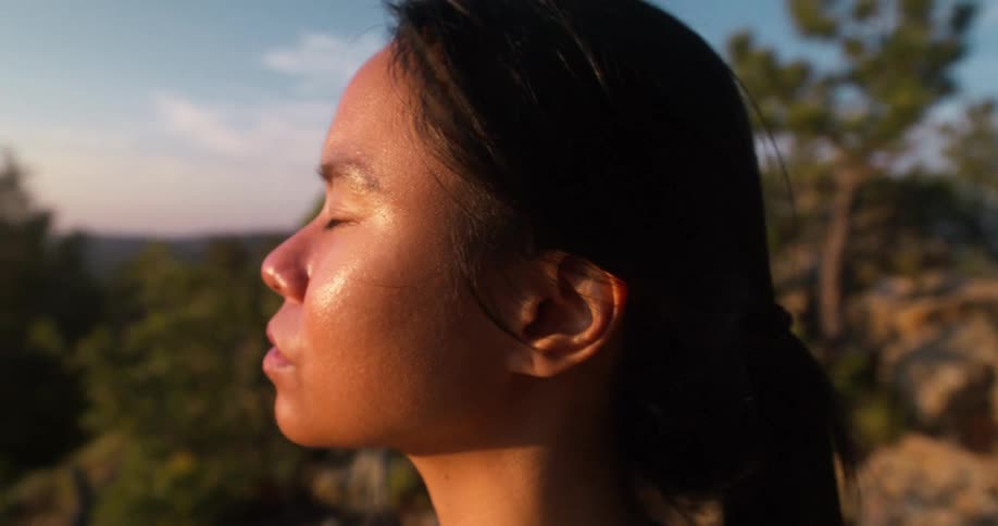 Woman has her eyes closed outdoors while the sun shines on her