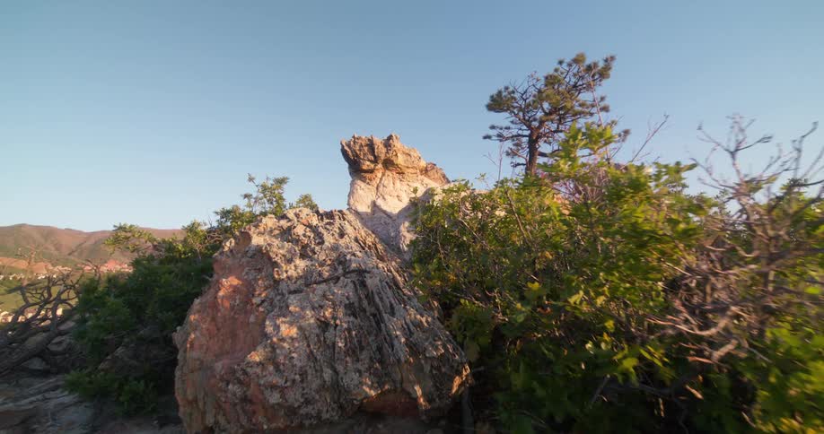 Sunlit rock formation and tree stand atop a rugged hill under a clear blue sky