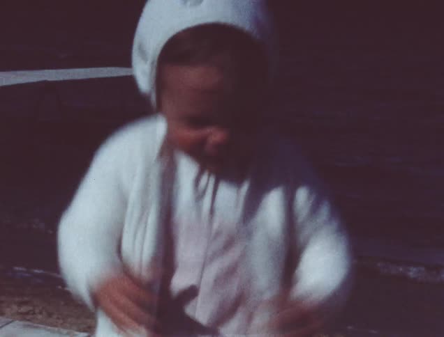 A toddler girl hops up and down near a lake