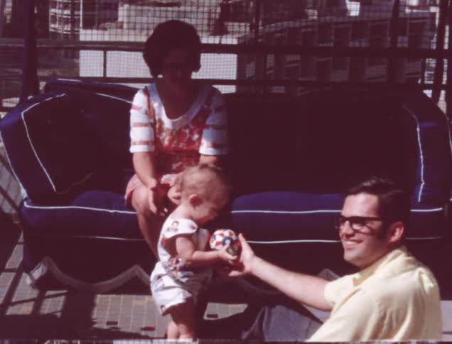 An older film of a woman and children outside near and on a porch glider
